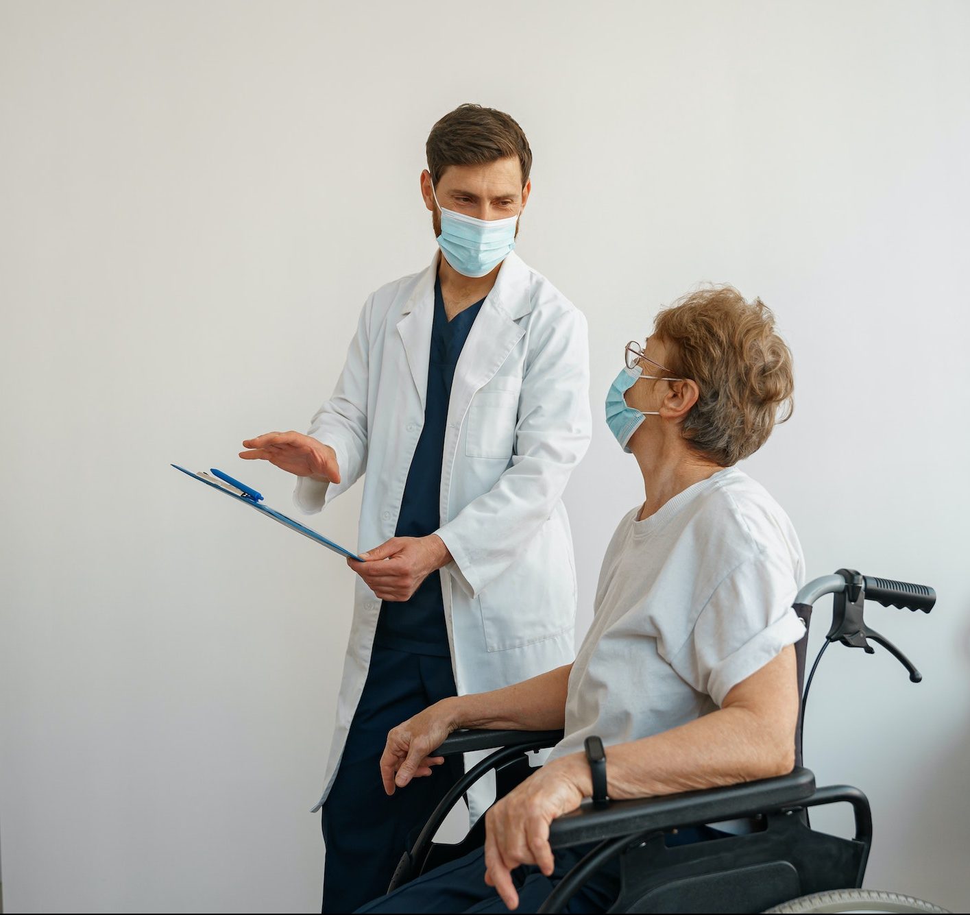 Doctor in mask explaining to a sick patient in a wheelchair the details of treatment